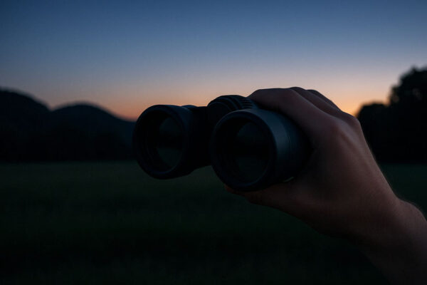 Ab wann ein Fernglas für die Dämmerung geeignet ist Fernglas in der Hand bei Sonnenuntergang – geeignet für die Dämmerung